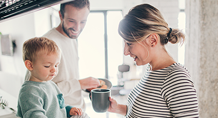 Pregnant mum smiling at her toddler son whilst he eats breakfast.