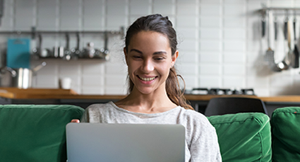 Young white woman smiling on sofa, looking at her laptop.