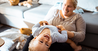 Young mum laughing and playing with her toddler over her knees