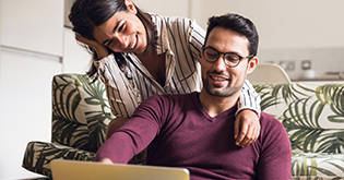 Young couple on sofa smiling whilst they look at a laptop